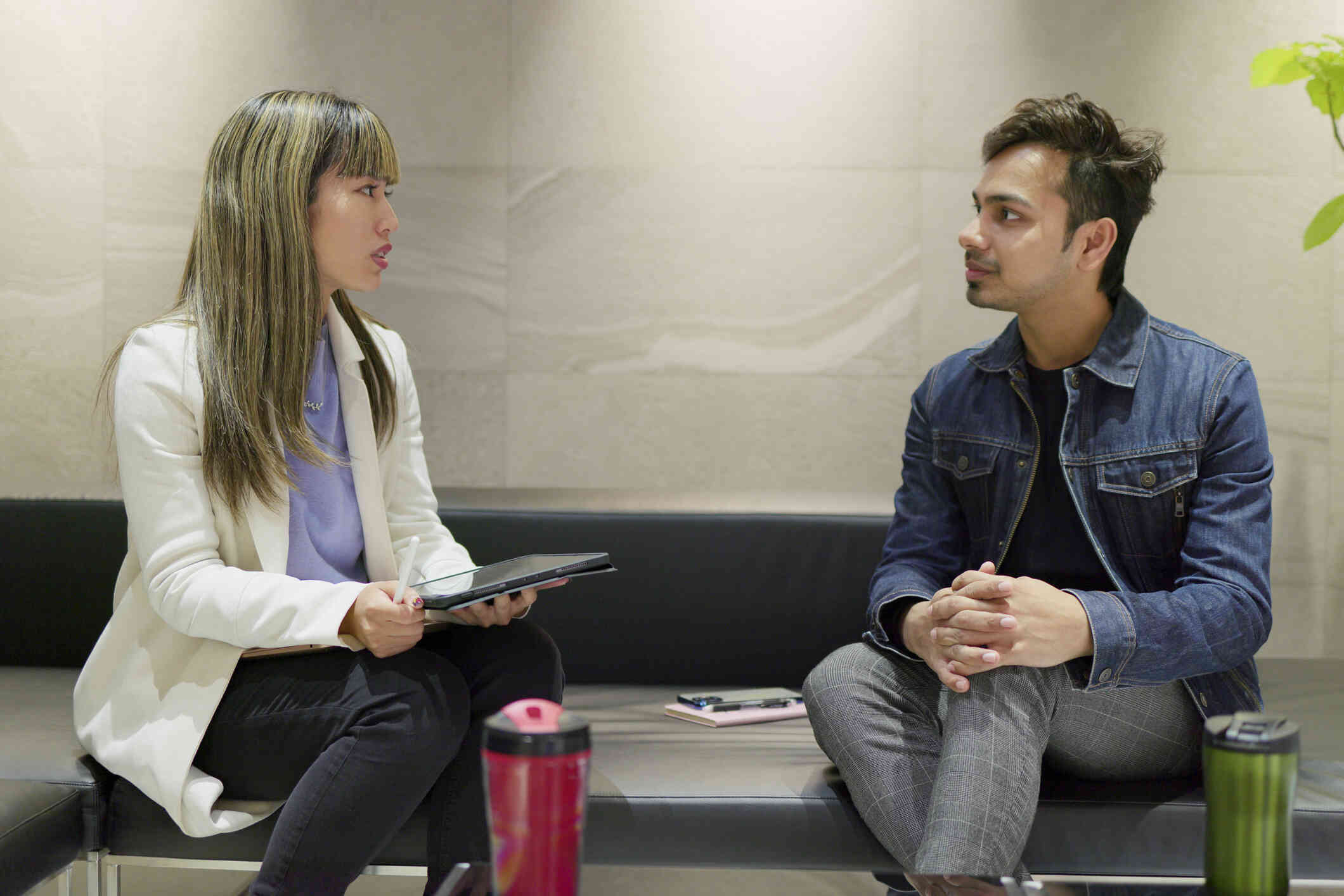 A man in a jean jacket sits next to his therapist as she talks during atherapy session.